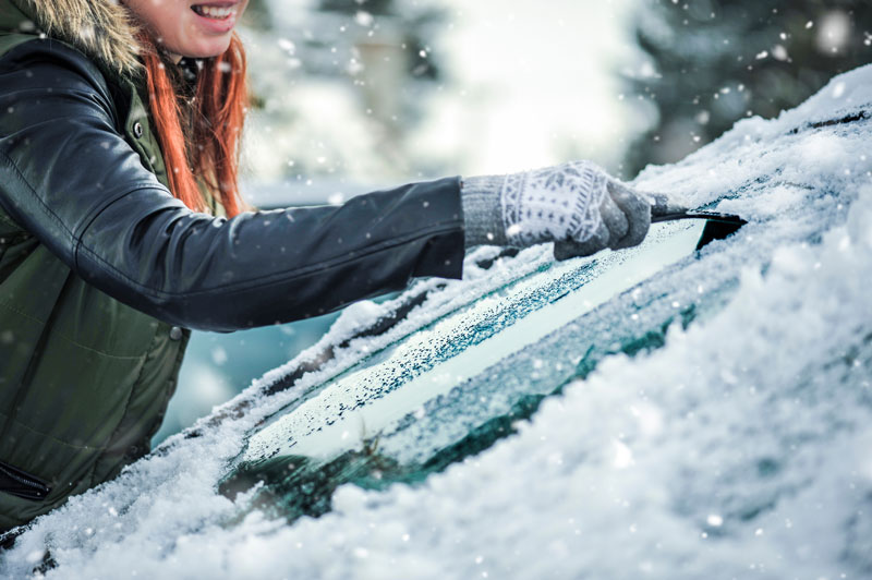 a woman removing snow from her car’s windshield
